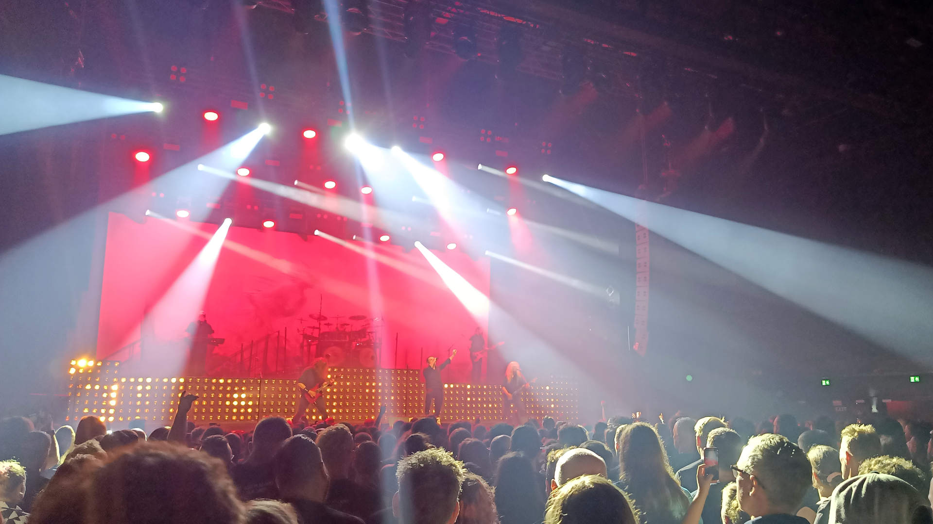 Audience in front of a stage. Band on stage. Spotlights on the audience. Stage lights are red/orange-ish