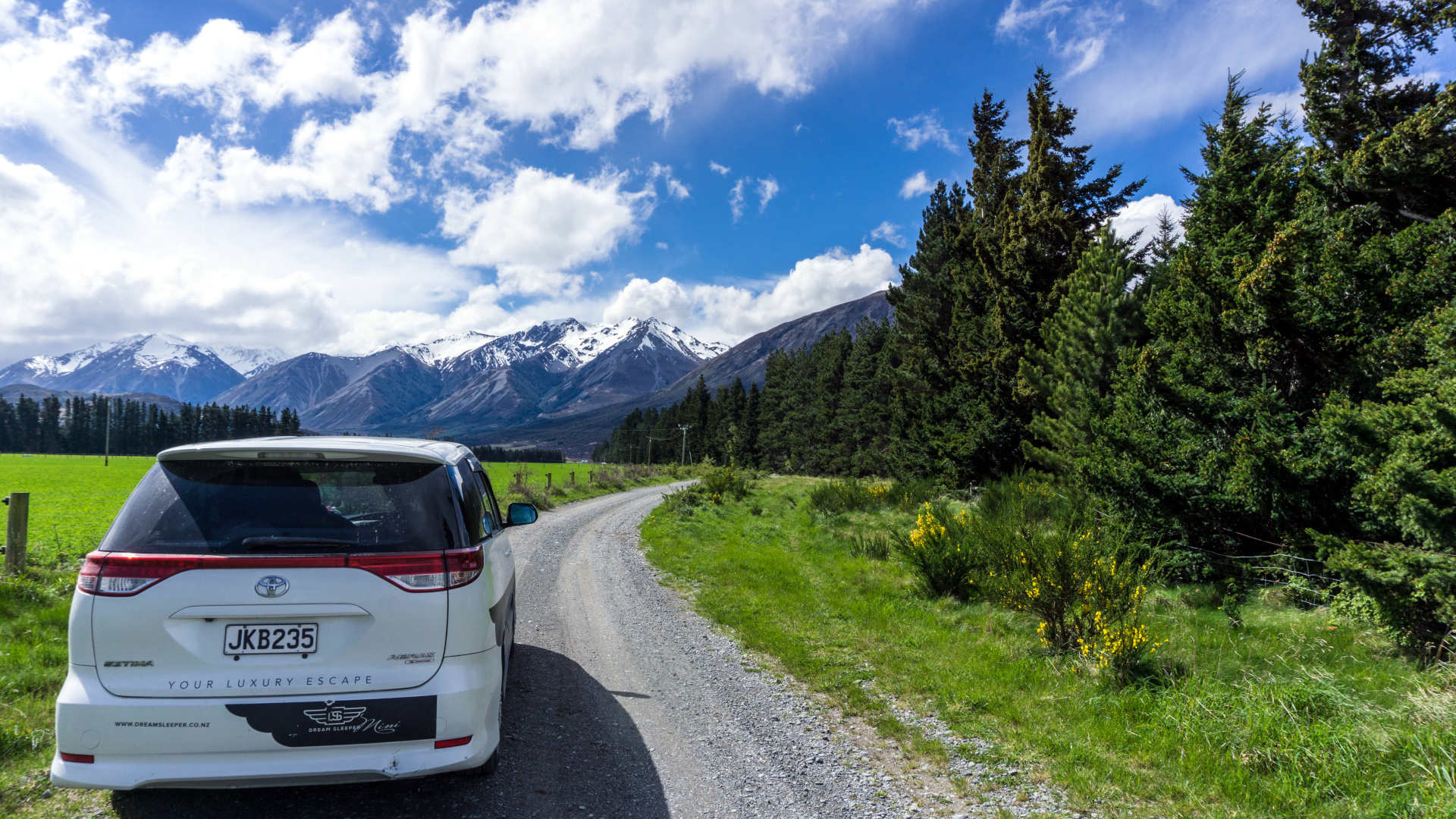Campervan on a gravel road driving towards mountains/hills on a sunny day (blue sky)