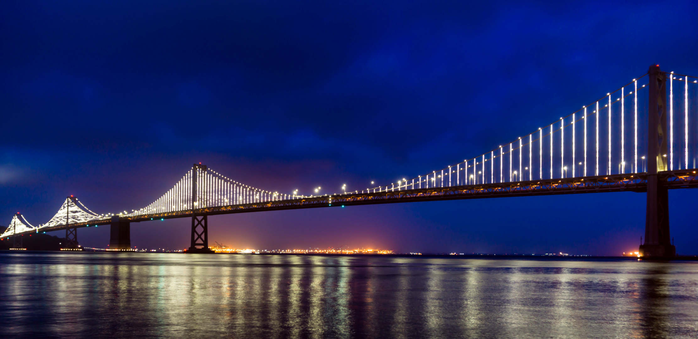 Long bridge by night - bridge is illuminated, city lights in the background